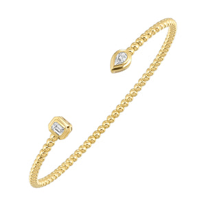 This delicate yellow gold bangle, culminating in an emerald and pear-shaped diamond, exudes contemporary femininity. The beaded details enhance its allure, creating a timeless piece of art.